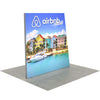 Side view of 8ft Angled Firefly Lightbox with illuminated coastal scene showing bright buildings and calm water, displayed on grey flooring for event presentation.
